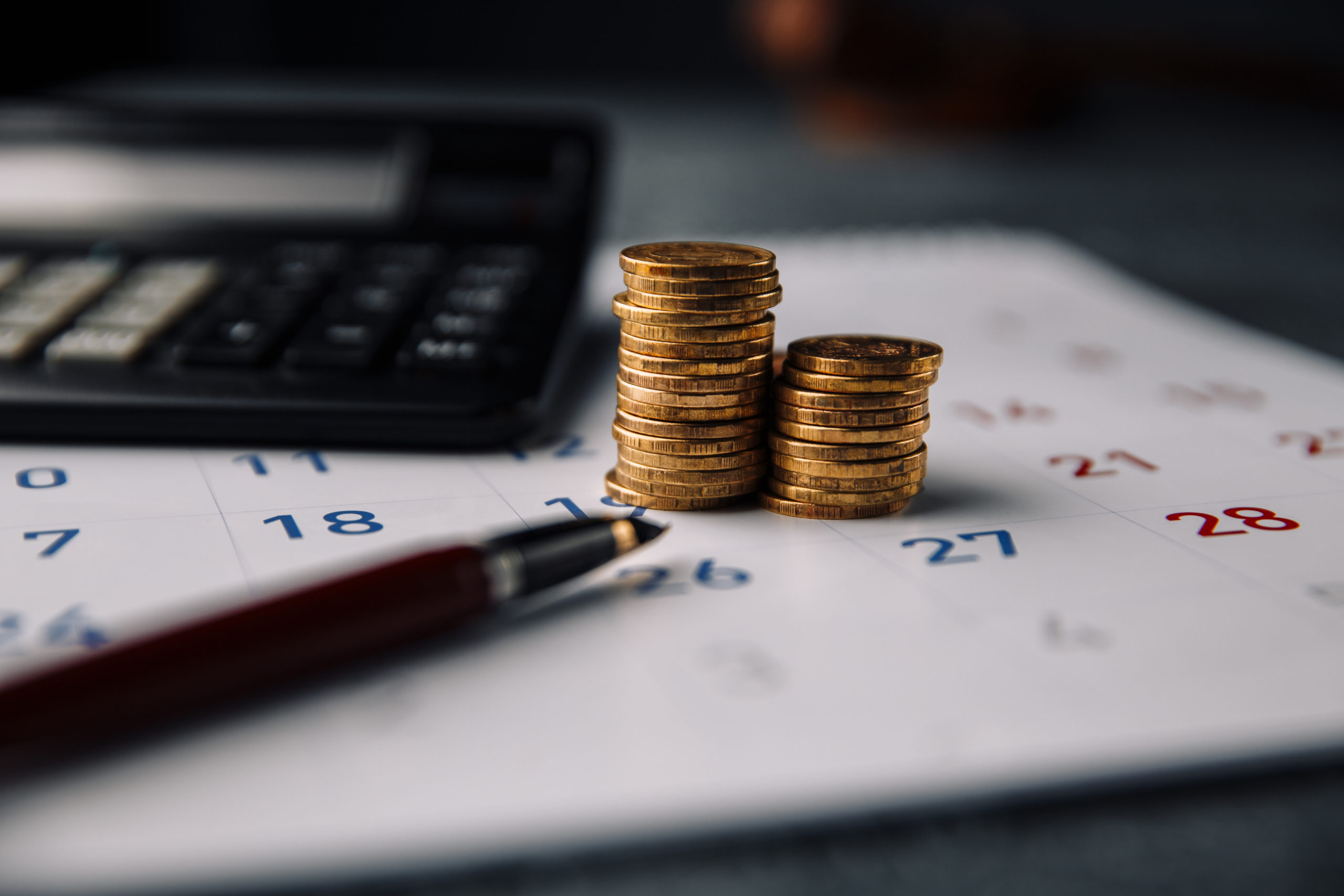 Calendar, Calculator And Stack Of Coins In A Office - Contabilidade em Santa Catarina | Amaral Contabilidade
